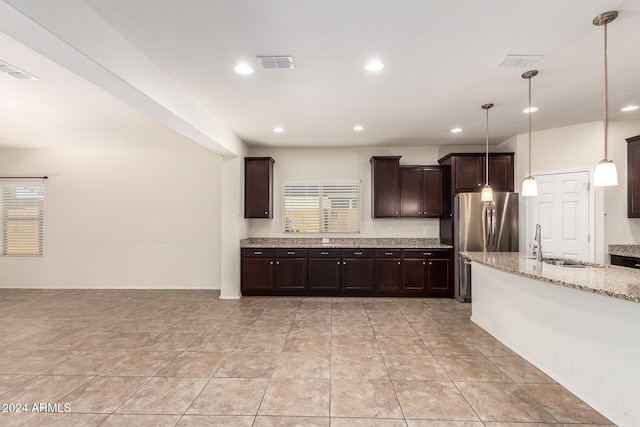 kitchen with sink, dark brown cabinets, stainless steel fridge, pendant lighting, and light stone counters