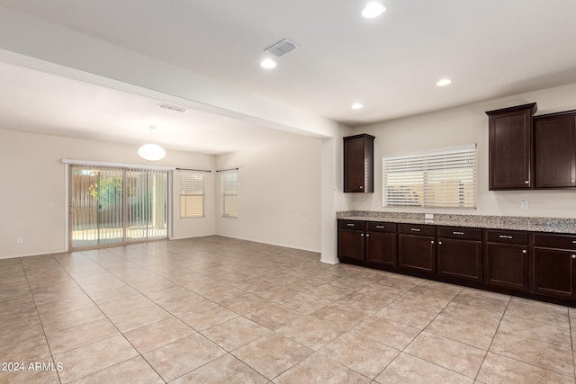 kitchen featuring light stone counters, dark brown cabinets, a healthy amount of sunlight, and light tile patterned floors