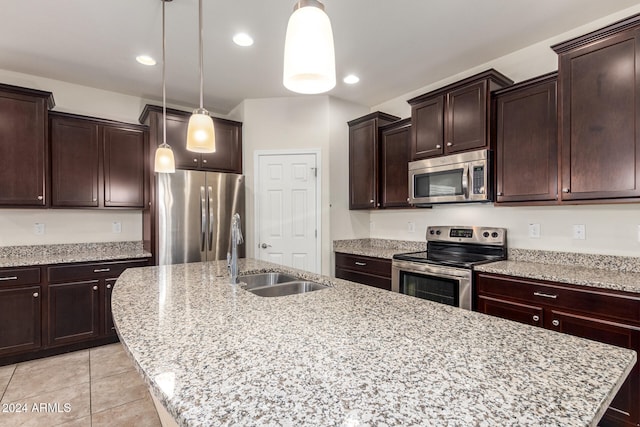 kitchen featuring hanging light fixtures, a kitchen island with sink, stainless steel appliances, sink, and light stone counters