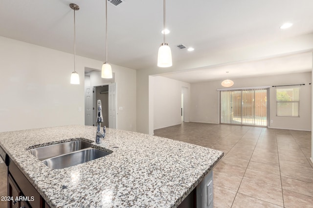 kitchen with sink, decorative light fixtures, light stone counters, light tile patterned floors, and a kitchen island with sink