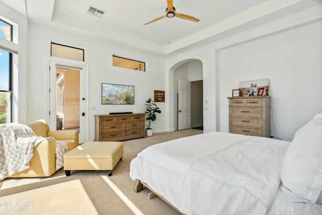 bedroom with visible vents, a raised ceiling, arched walkways, light colored carpet, and a towering ceiling