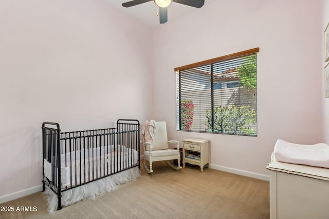 carpeted bedroom featuring a nursery area, baseboards, and a ceiling fan