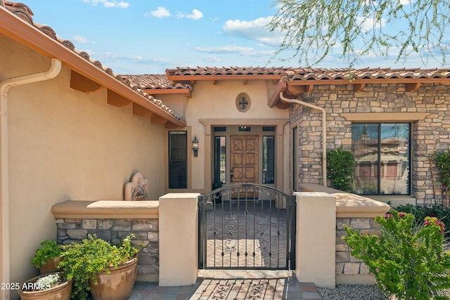 view of exterior entry with stone siding, a gate, fence, and stucco siding