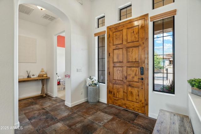 entryway featuring stone tile floors, visible vents, arched walkways, and baseboards