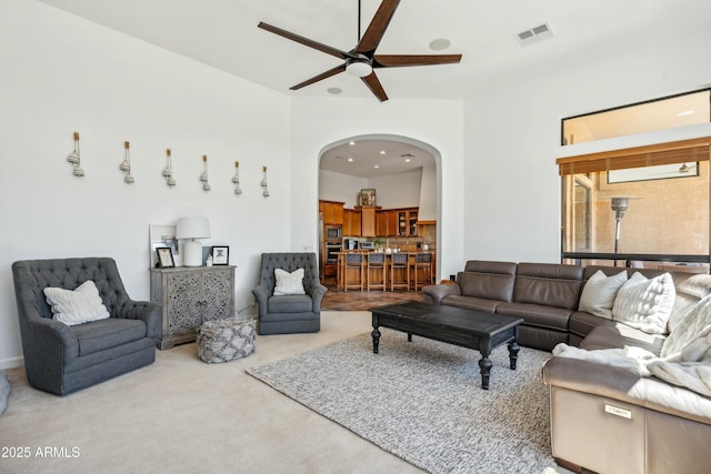 carpeted living room with a ceiling fan, arched walkways, and visible vents