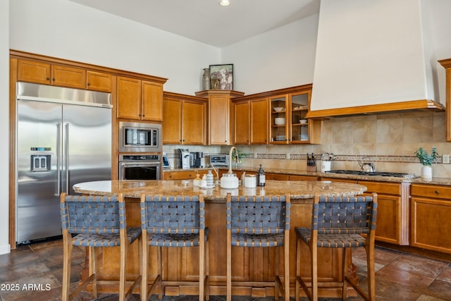 kitchen with built in appliances, backsplash, light stone countertops, and brown cabinets