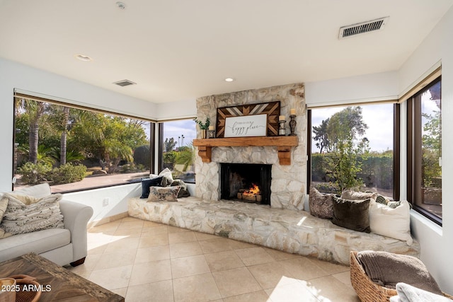 living room featuring a stone fireplace, a healthy amount of sunlight, and light tile patterned flooring