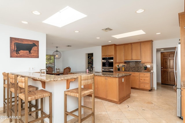 kitchen with kitchen peninsula, light stone counters, a kitchen island with sink, stainless steel refrigerator, and a breakfast bar area