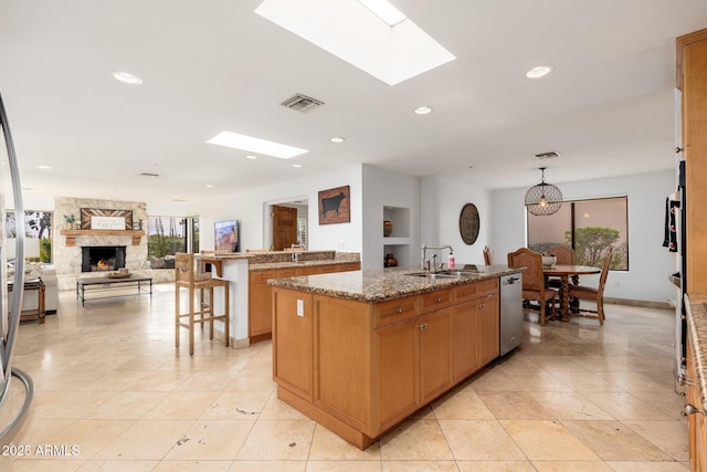 kitchen featuring a skylight, light stone countertops, hanging light fixtures, stainless steel dishwasher, and a center island with sink