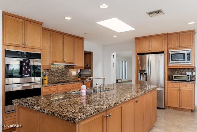 kitchen featuring backsplash, a kitchen island with sink, sink, and appliances with stainless steel finishes