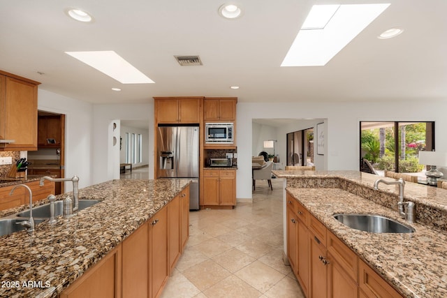 kitchen with light stone countertops, appliances with stainless steel finishes, a skylight, and sink