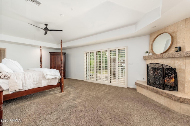 carpeted bedroom with a tile fireplace, access to outside, a tray ceiling, and ceiling fan