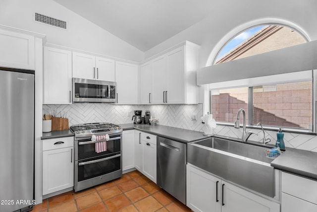 kitchen featuring visible vents, dark countertops, vaulted ceiling, a sink, and stainless steel appliances