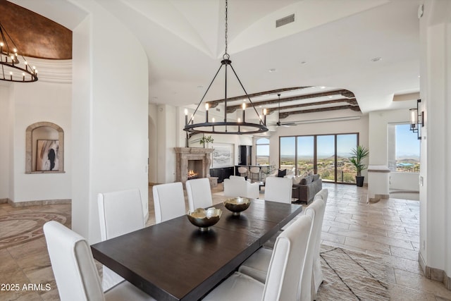 dining room featuring stone tile floors, a notable chandelier, visible vents, vaulted ceiling, and a lit fireplace