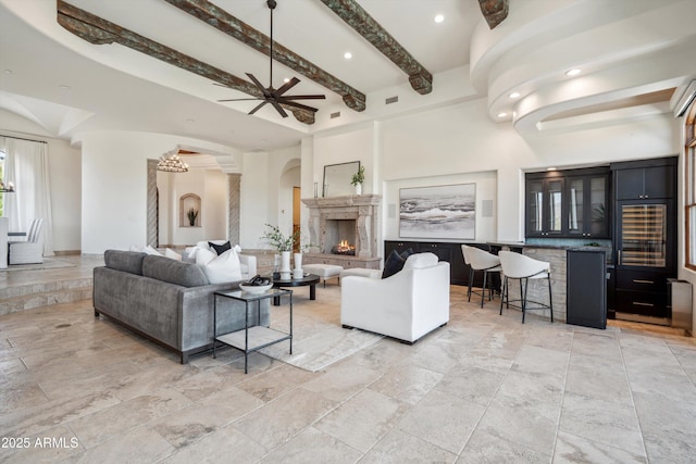 living room with beam ceiling, stone tile floors, indoor bar, a high end fireplace, and arched walkways