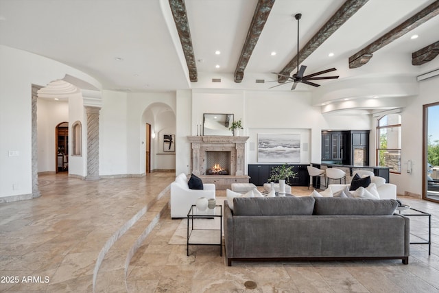 living room with beamed ceiling, ceiling fan, a high end fireplace, baseboards, and arched walkways