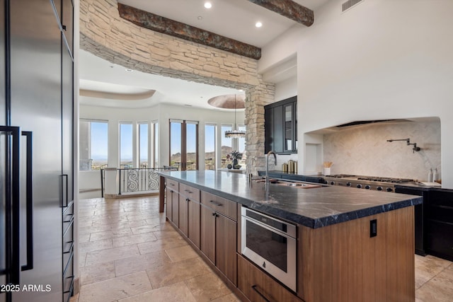 kitchen with a sink, stainless steel appliances, glass insert cabinets, visible vents, and an island with sink
