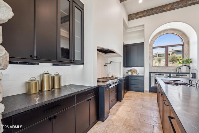 kitchen featuring a sink, stainless steel appliances, glass insert cabinets, stone tile floors, and tasteful backsplash