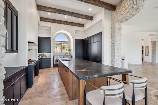 kitchen featuring arched walkways, a spacious island, a sink, beam ceiling, and a towering ceiling