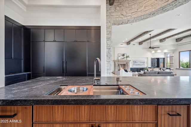 kitchen featuring dark stone counters, beamed ceiling, a sink, ceiling fan, and open floor plan