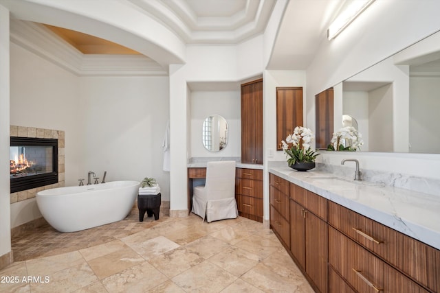 full bathroom featuring crown molding, a tiled fireplace, a freestanding tub, a towering ceiling, and vanity