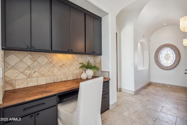 unfurnished office featuring arched walkways, vaulted ceiling, stone tile flooring, and baseboards