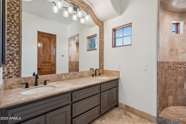 bathroom featuring double vanity, baseboards, tiled shower, and a sink