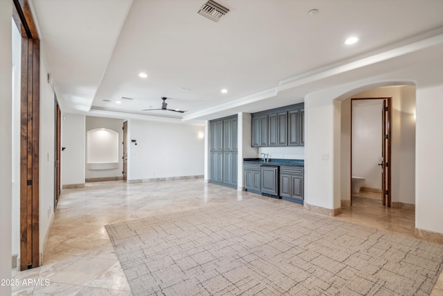 unfurnished living room featuring visible vents, a raised ceiling, ceiling fan, and arched walkways