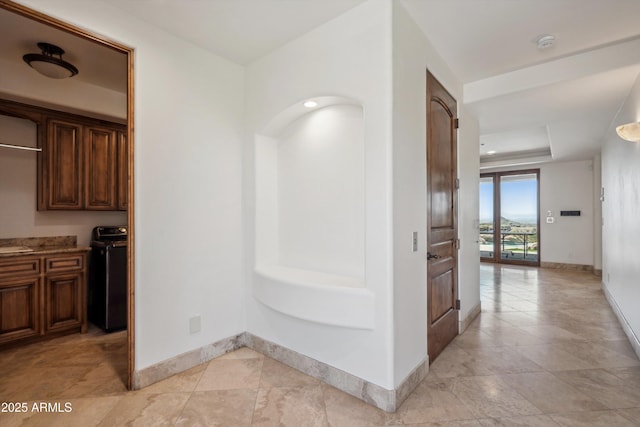 hall featuring baseboards, a raised ceiling, and light tile patterned flooring
