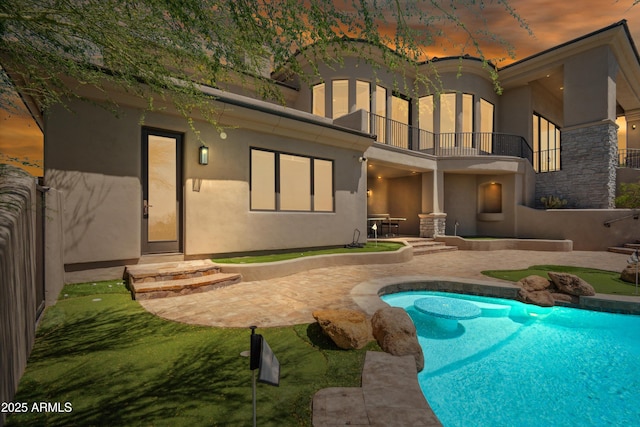 back of property featuring an outdoor pool, stucco siding, and a balcony