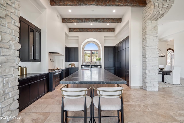 kitchen featuring an island with sink, a kitchen bar, a sink, ornate columns, and a high ceiling