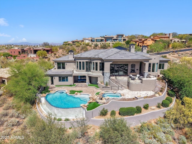 back of property featuring an outdoor pool, stucco siding, an in ground hot tub, and a chimney
