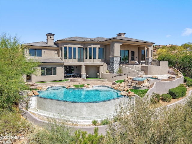 back of house featuring a patio area, a balcony, an outdoor pool, an in ground hot tub, and stucco siding