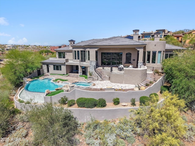 rear view of property featuring an in ground hot tub, an outdoor pool, a chimney, a patio area, and stucco siding