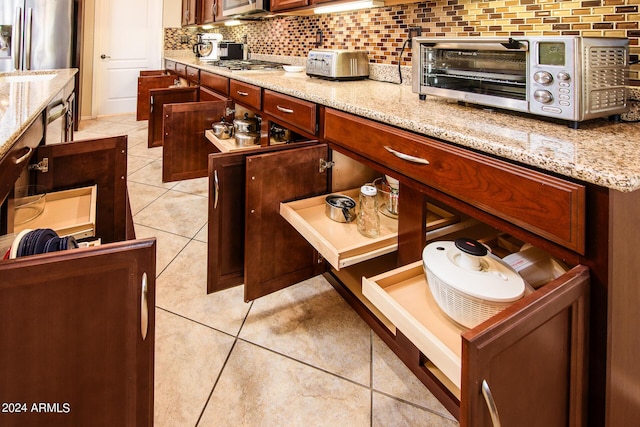 kitchen featuring light stone counters, light tile patterned floors, decorative backsplash, appliances with stainless steel finishes, and a toaster