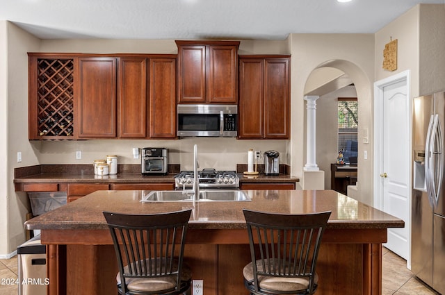 kitchen with appliances with stainless steel finishes, a center island with sink, decorative columns, and a breakfast bar area