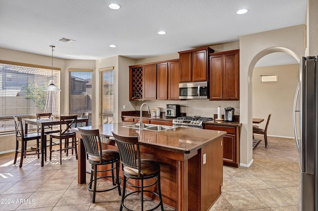 kitchen featuring appliances with stainless steel finishes, sink, light tile patterned floors, pendant lighting, and a center island with sink