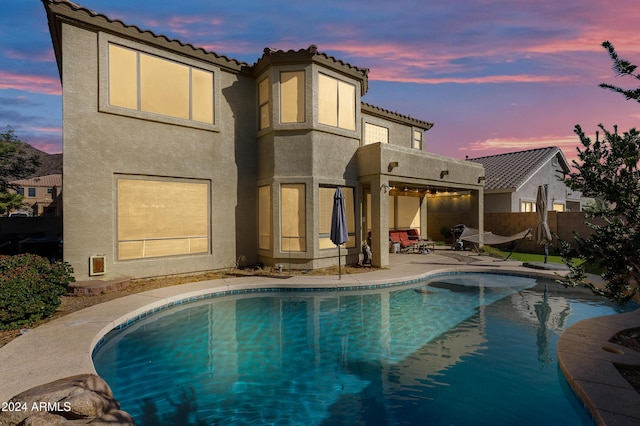 back house at dusk with a patio area, a fenced in pool, and a balcony