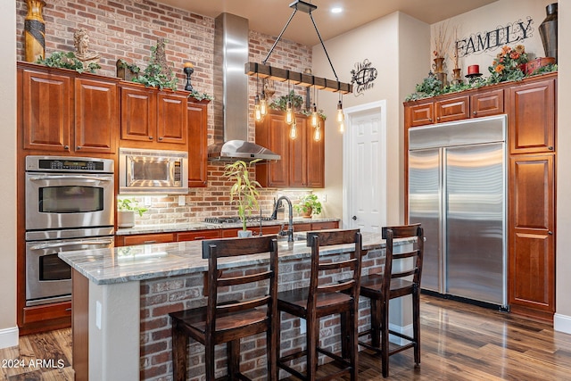 kitchen featuring extractor fan, a breakfast bar area, dark wood-type flooring, brick wall, and built in appliances