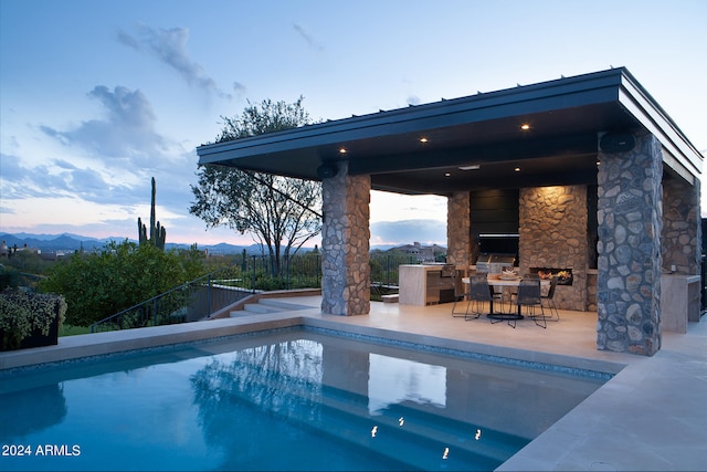 pool at dusk with a patio area and area for grilling