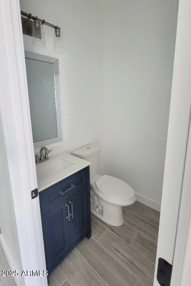 bathroom featuring toilet, baseboards, wood finish floors, and vanity