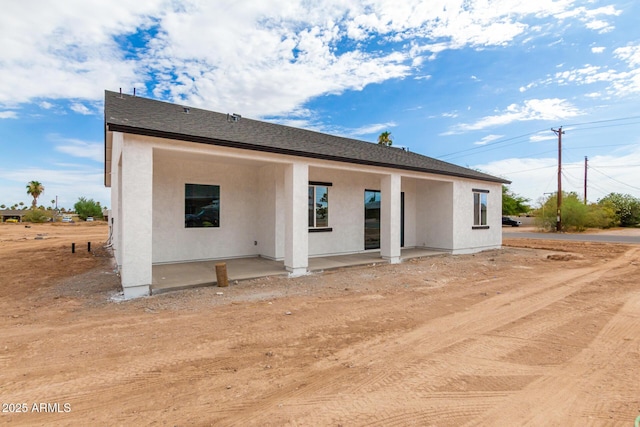 back of house with a shingled roof, a patio area, and stucco siding