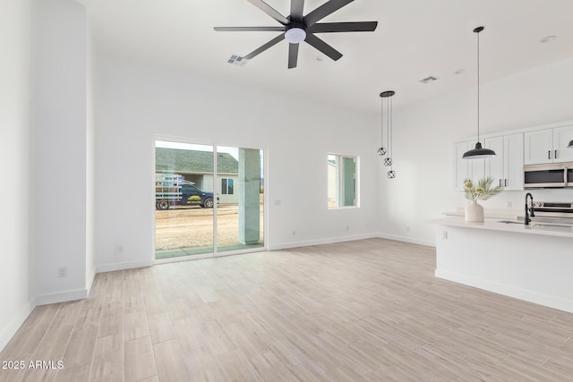 unfurnished living room featuring light wood-style floors, a sink, baseboards, and a ceiling fan