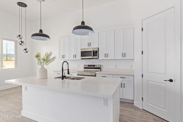 kitchen with a kitchen island with sink, stainless steel appliances, white cabinetry, hanging light fixtures, and light countertops