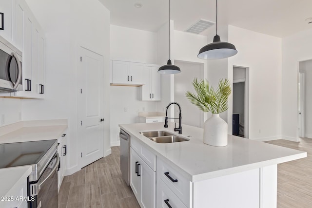 kitchen with visible vents, white cabinets, an island with sink, decorative light fixtures, and a sink