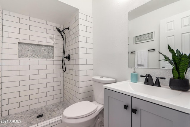 bathroom featuring a tile shower, vanity, and toilet