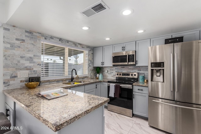 kitchen with gray cabinetry, light stone countertops, sink, kitchen peninsula, and appliances with stainless steel finishes