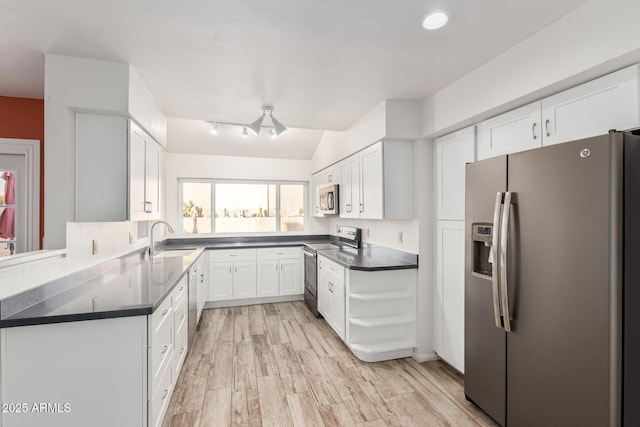 kitchen with stainless steel appliances, dark countertops, light wood-style floors, white cabinets, and a sink