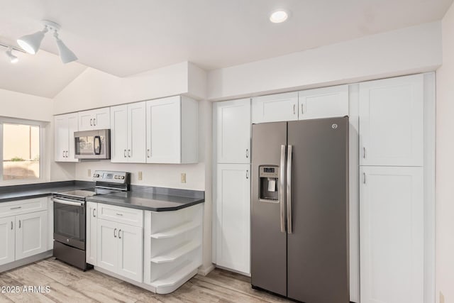 kitchen featuring white cabinetry, vaulted ceiling, appliances with stainless steel finishes, light wood finished floors, and dark countertops