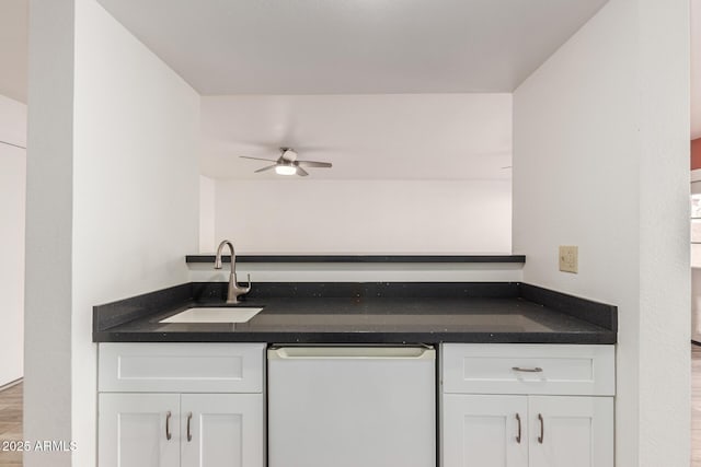 kitchen featuring dark countertops, white cabinetry, a sink, and dishwasher